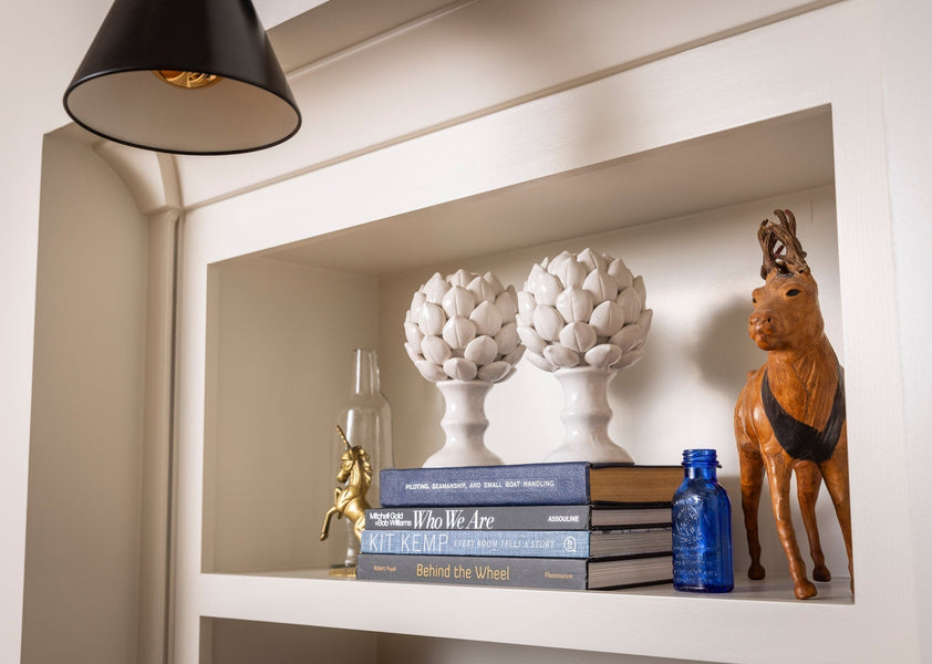 Shelf vignette with white ceramic finials, stacked books, cobalt bottle and leather deer figure
