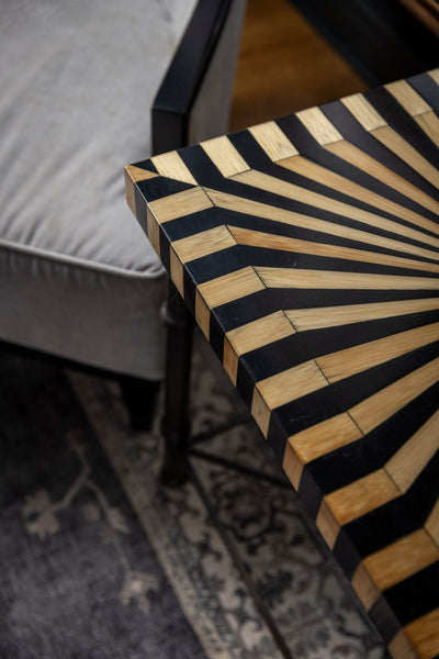 Sunburst straw marquetry table corner in black lacquer beside a pale chair and faded rug