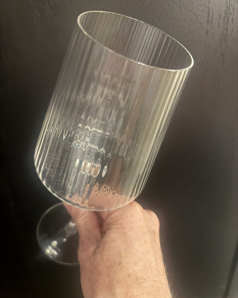 A hand holding a fluted Bandol glass up to the light, rim edge catching as a bright line
