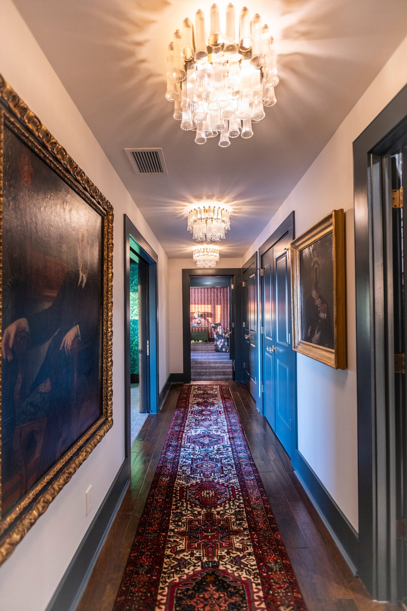 Long corridor with tiered glass chandeliers and gilt-framed portraits along a runner