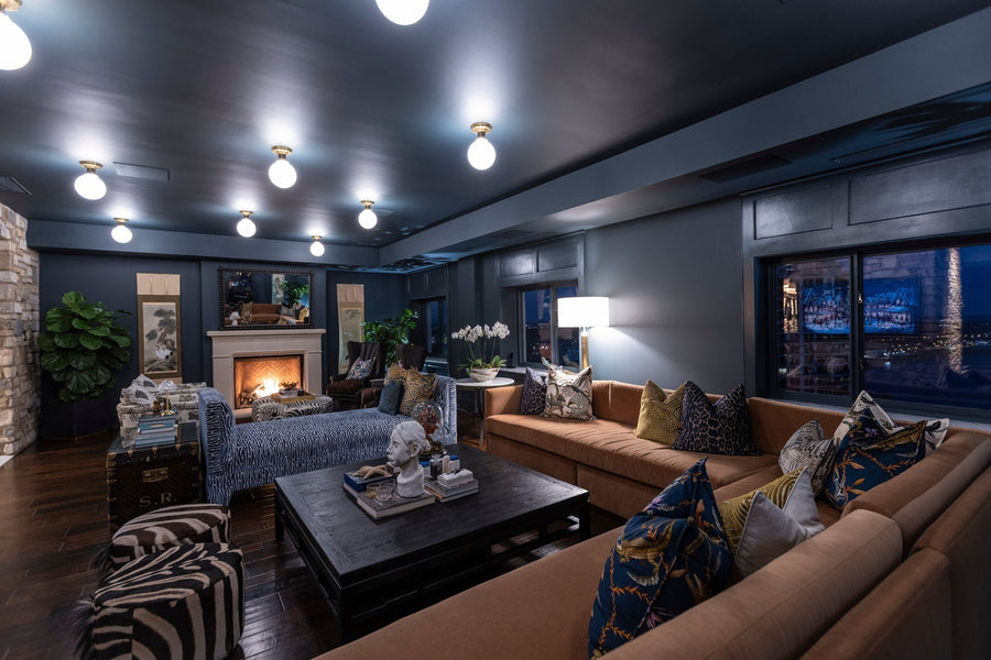 Night living room with camel sectional, lit fireplace, opal globe ceiling lights and a shaded floor lamp