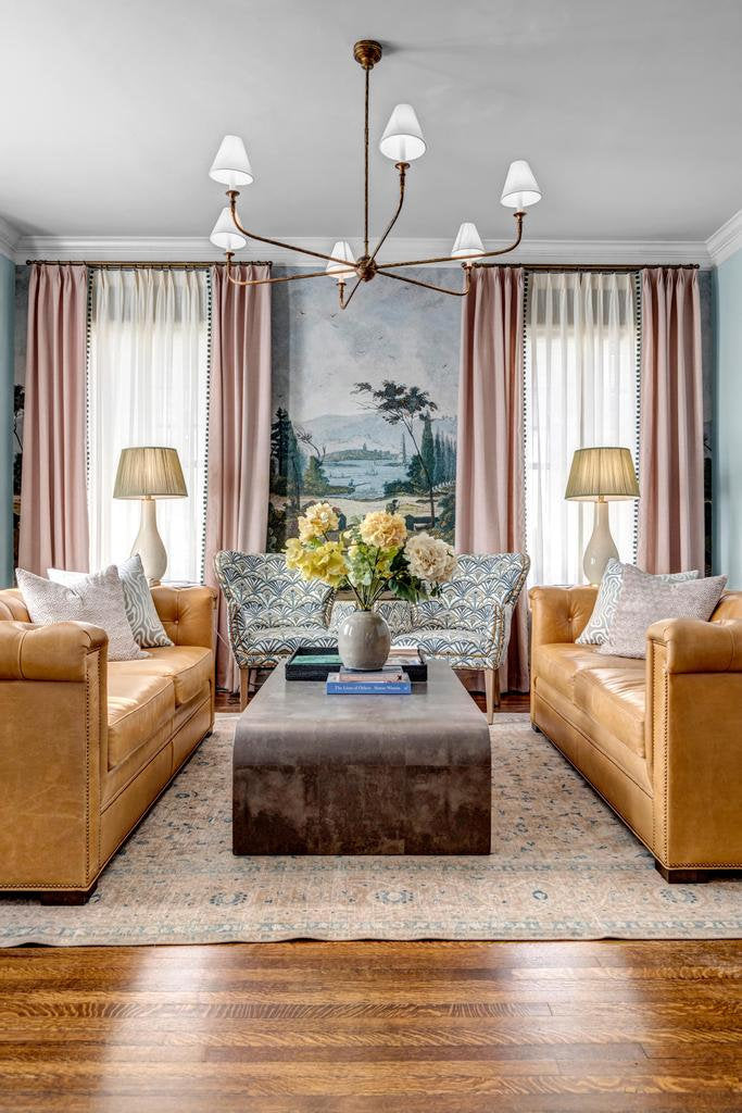 Symmetrical living room with two tan leather sofas, a fan-print settee and a scenic mural