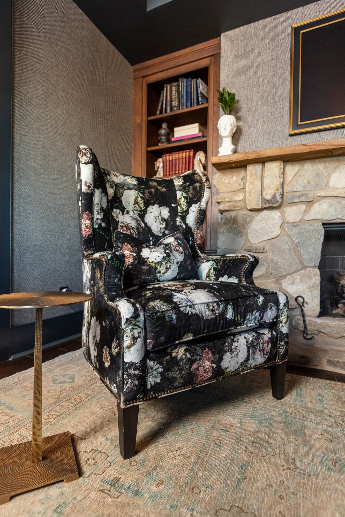 Dark floral velvet wingback chair with brass nailhead trim beside a brass drink table