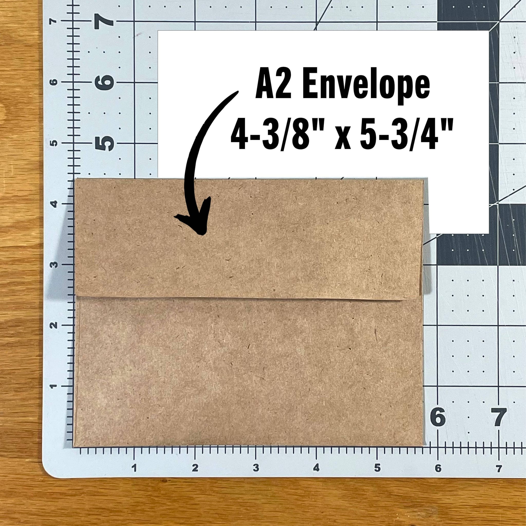 Kraft brown A2 envelope, closed flap-up, resting on gridded cutting mat