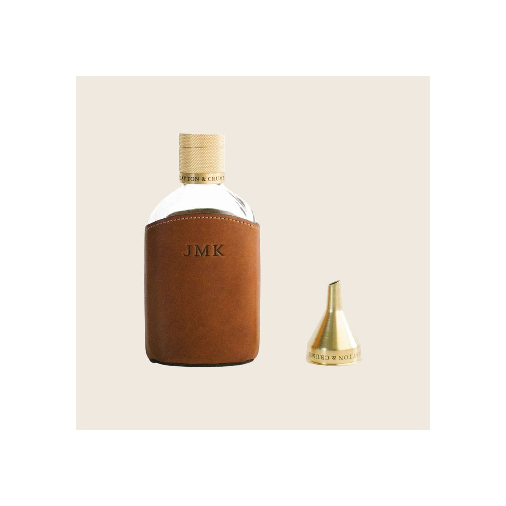 Glass flask in tan leather sleeve with brass knurled cap and small brass funnel accessory