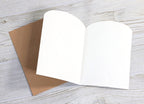 Greeting card open flat showing blank white interior pages with kraft brown cover on whitewashed wood surface