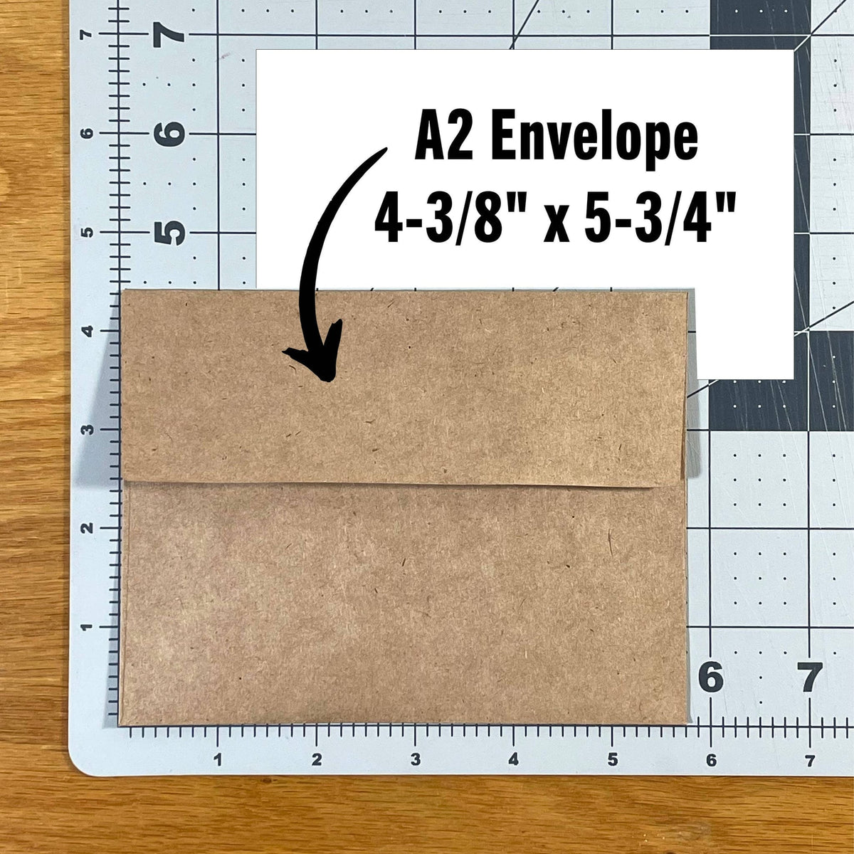 Kraft brown A2 envelope, closed flap-up, resting on gridded cutting mat