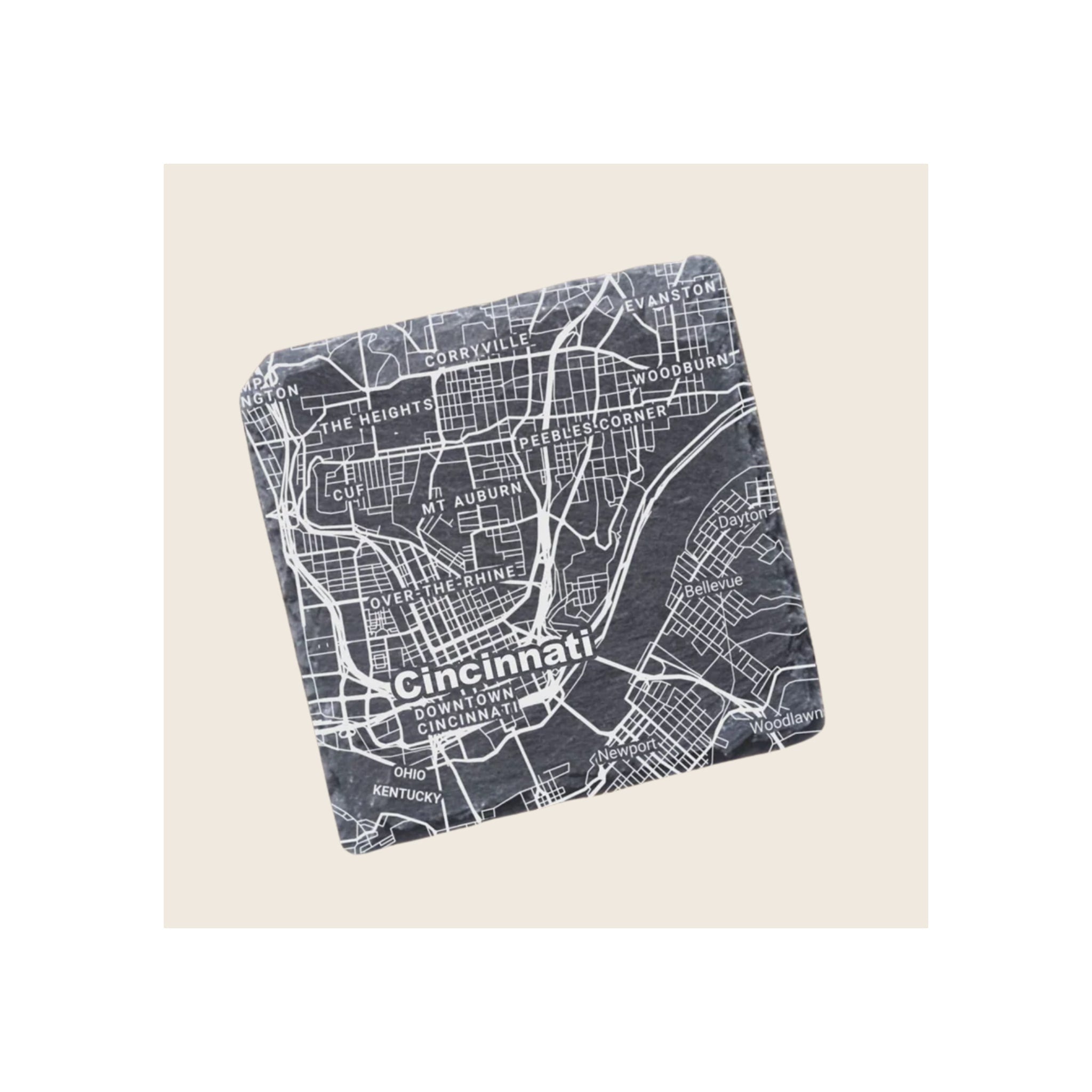 Square slate coaster engraved with white Cincinnati city map, angled view on beige background