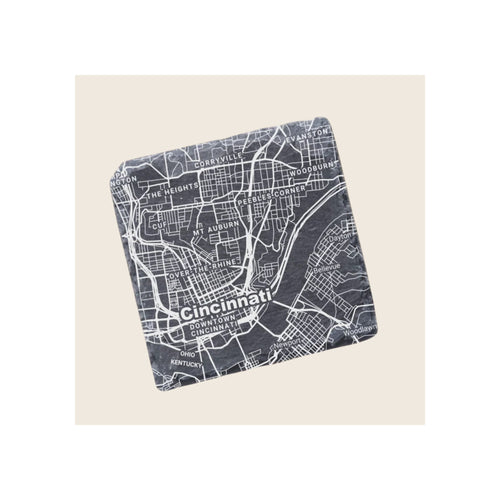 Square slate coaster engraved with white Cincinnati city map, angled view on beige background