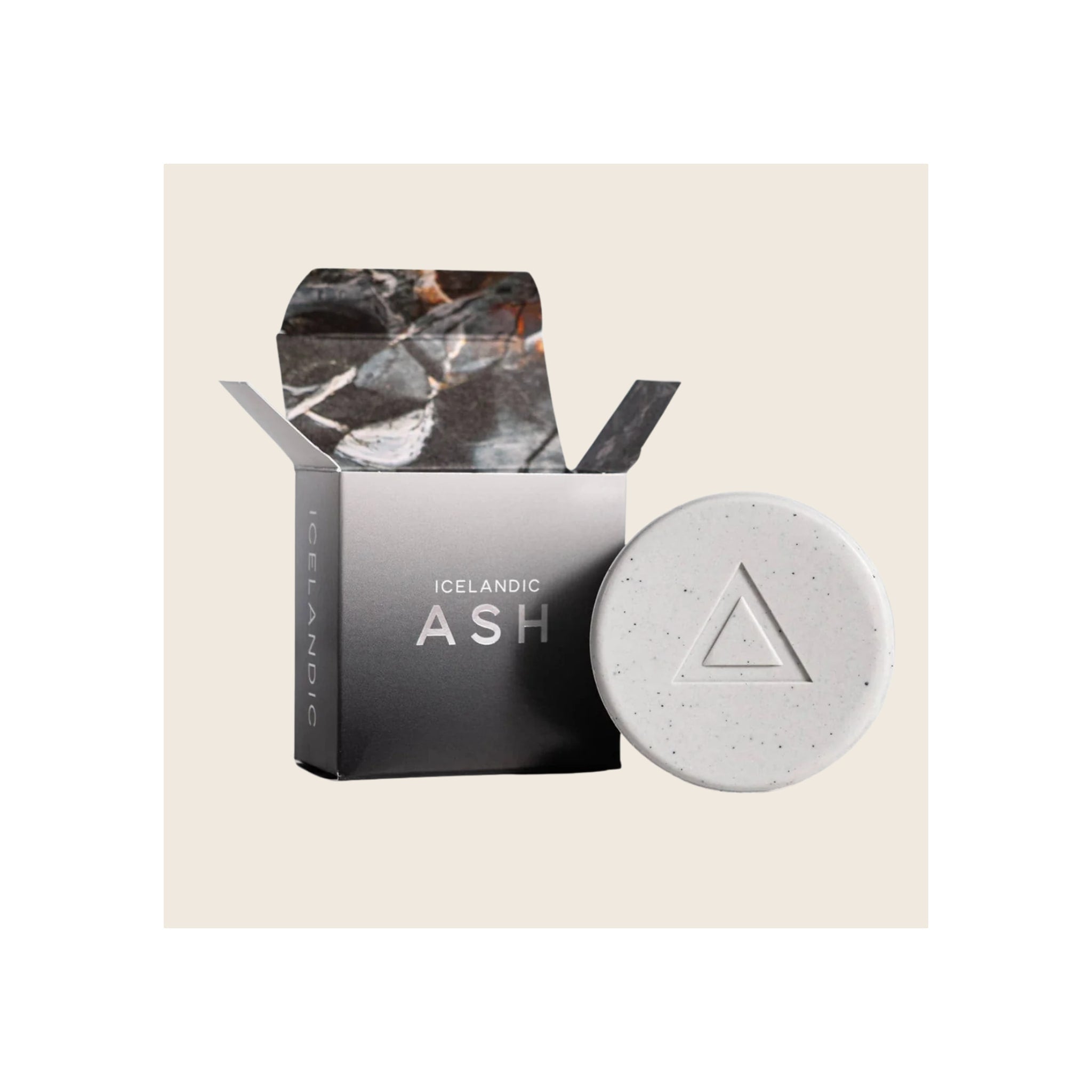 Round white speckled volcanic ash soap bar with triangle emboss beside open black branded box