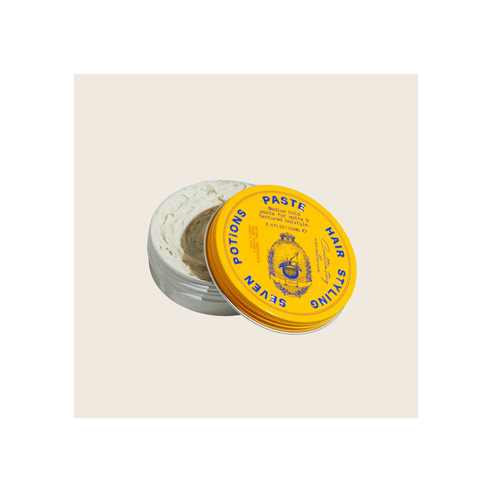 Hair styling paste tin, open lid leaning against jar, yellow with blue text, white cream product visible