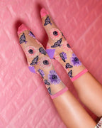 Sheer crew socks with pink and purple floral and butterfly print, worn on raised feet against pink background