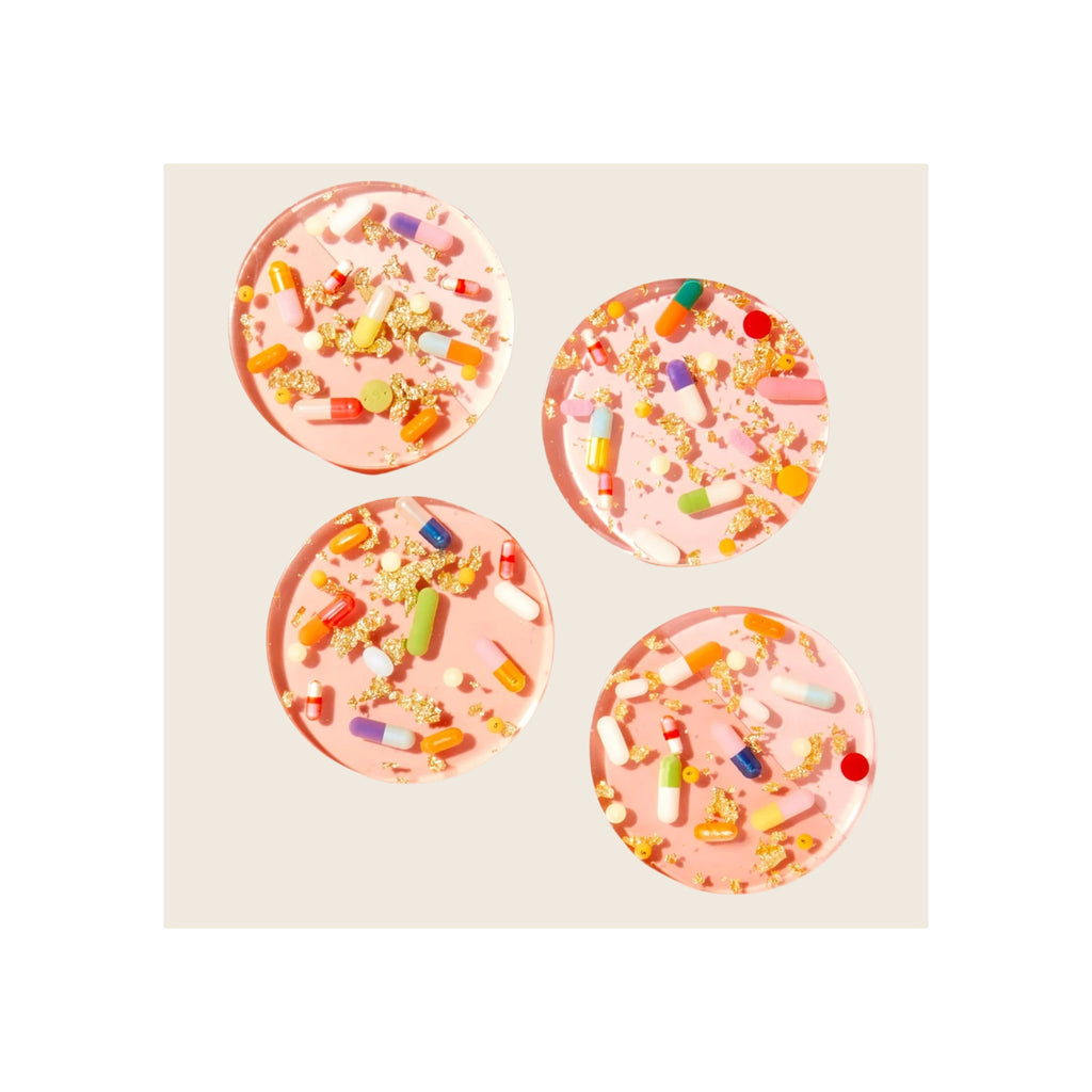 Four round pink resin coasters with embedded colorful pill capsules and gold foil flakes, overhead flat-lay view