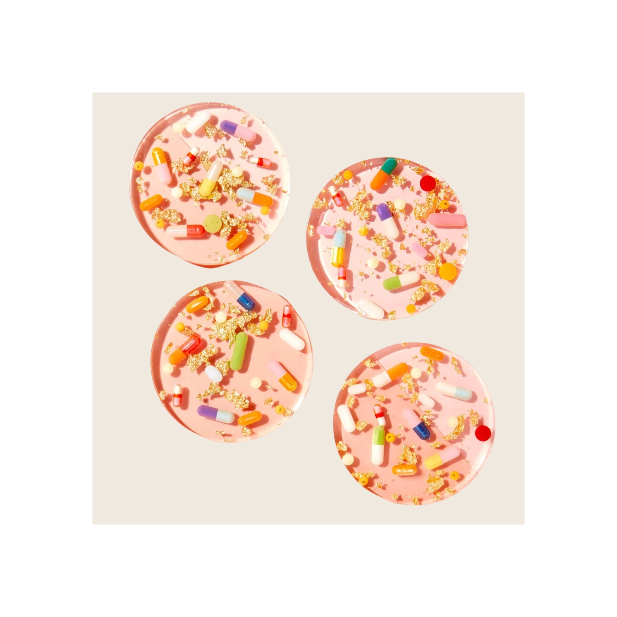 Four round pink resin coasters with embedded colorful pill capsules and gold foil flakes, overhead flat-lay view