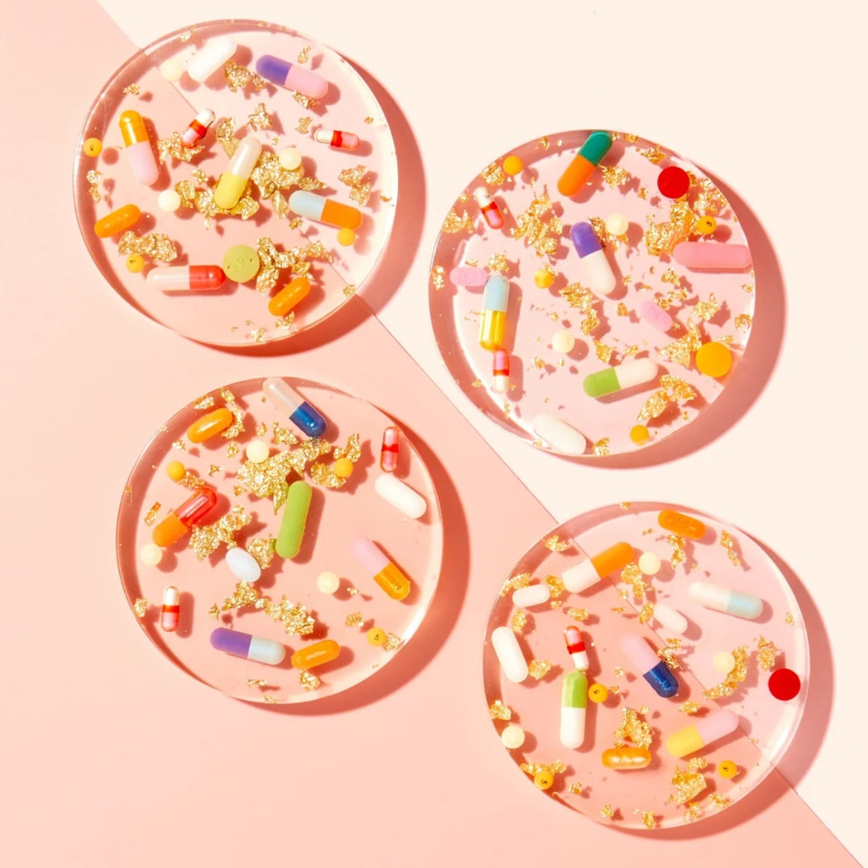 Four round pink resin coasters with embedded colorful capsules and gold foil flakes, flat-lay arrangement