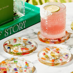 Round clear resin coasters with embedded colorful pill capsules and gold leaf flakes, set on marble surface