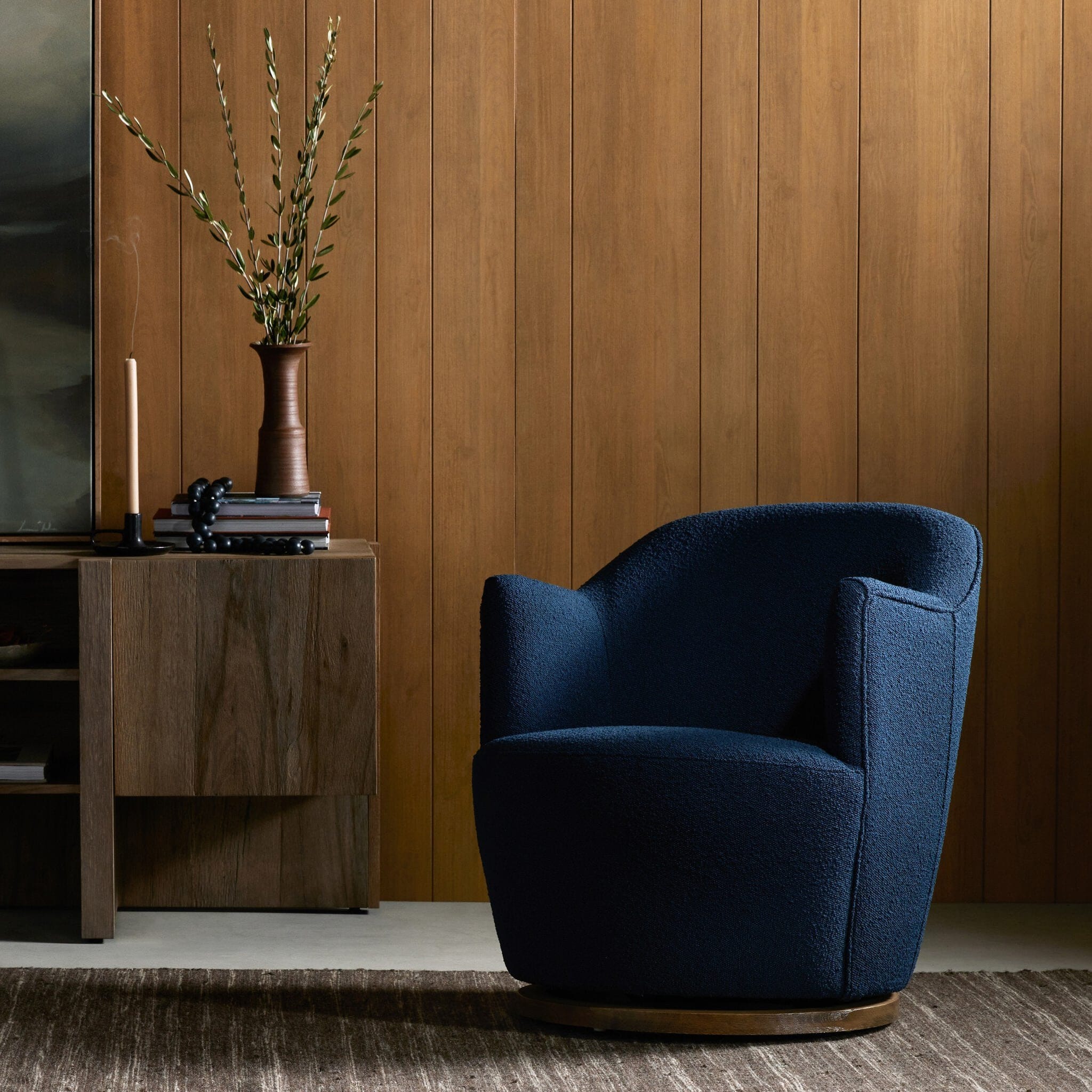 Navy bouclé swivel chair styled in warm wood-paneled living room beside media console and ceramic vase
