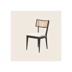 Dining chair with black wood frame, natural cane back panel, and white upholstered seat cushion, angled three-quarter view