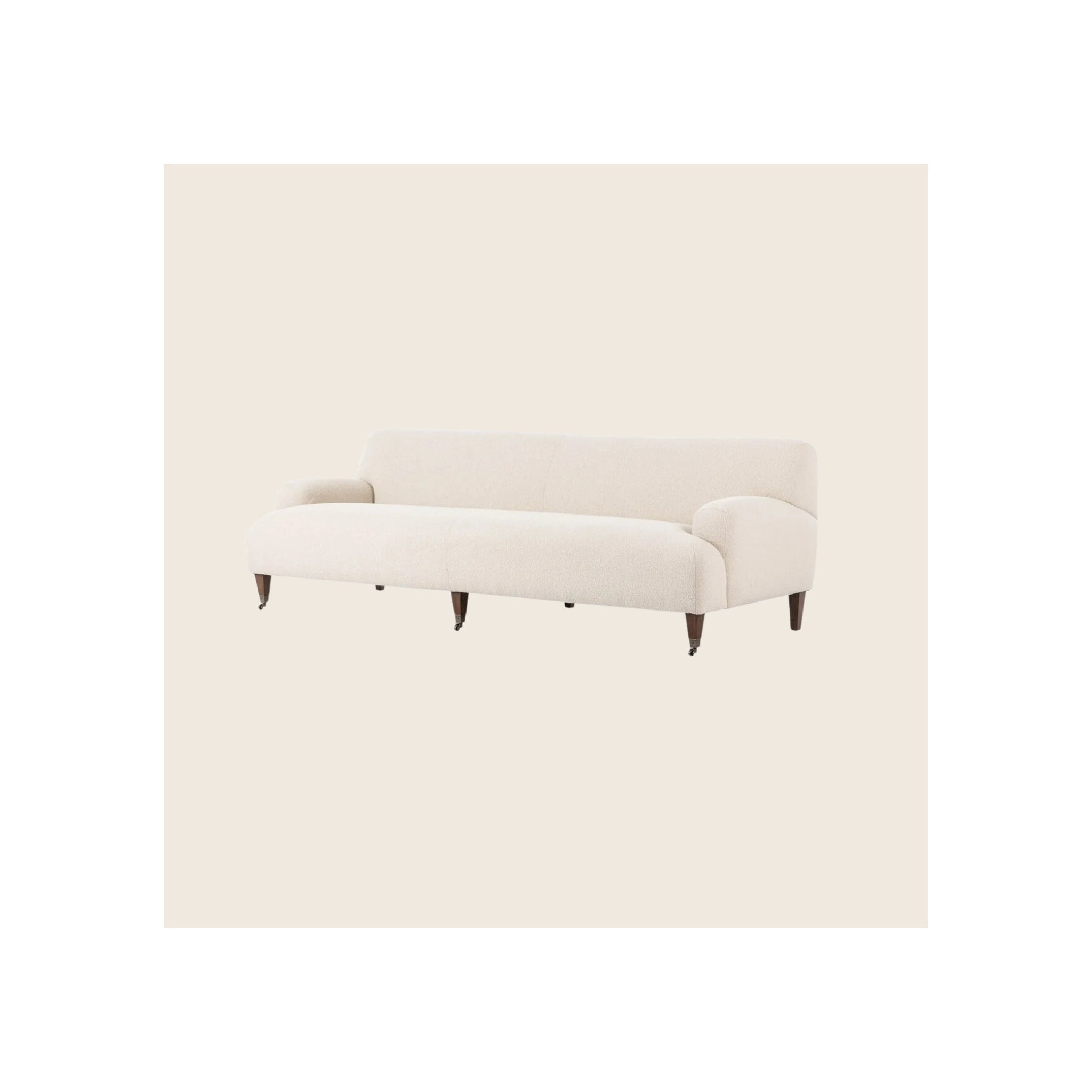 Sofa in cream bouclé fabric with dark walnut tapered legs and caster wheels, angled view