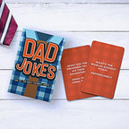Dad Jokes card game box with two orange joke cards displayed on white wood surface