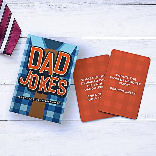 Dad Jokes card game box with two orange joke cards displayed on white wood surface