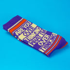 Folded crew socks in purple, cream, and orange stripes with novelty slogan text, on blue background
