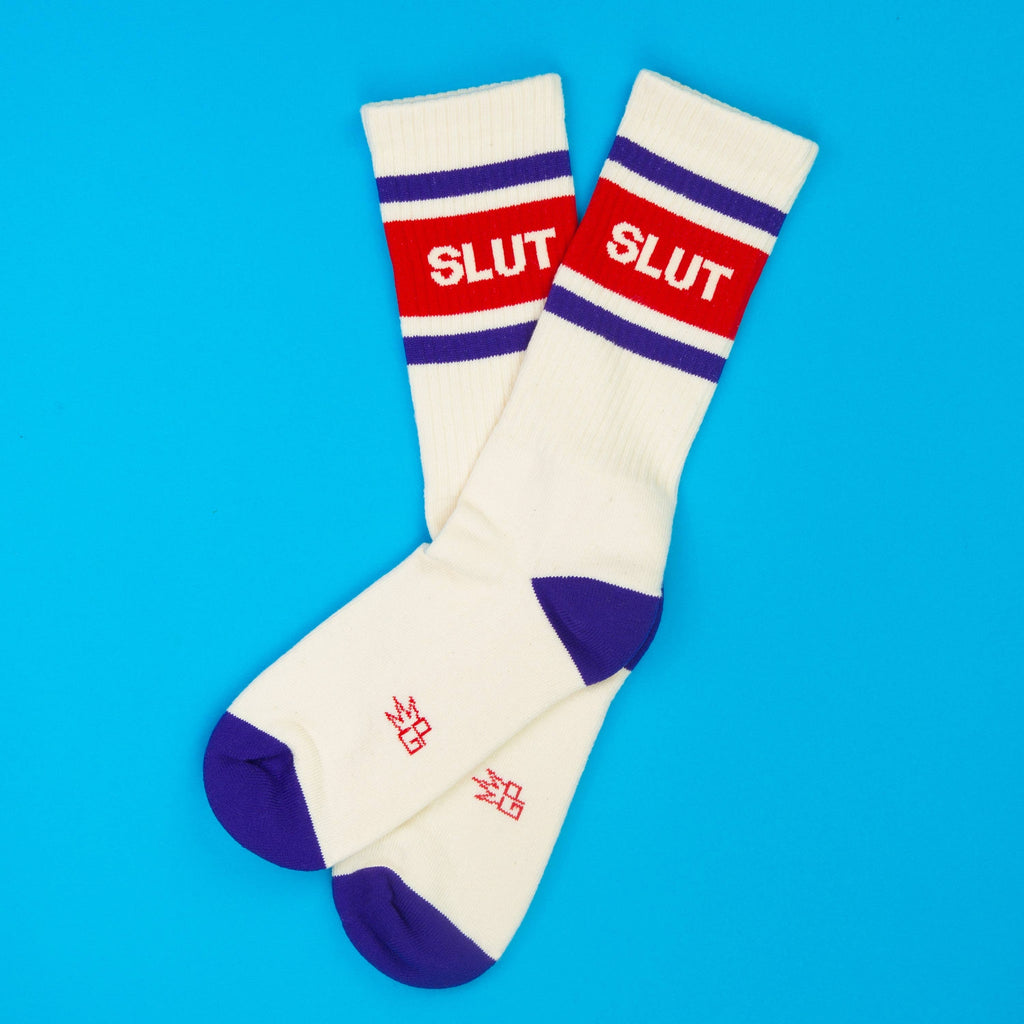 Crew socks, white knit with purple heel and toe, red stripe reading SLUT, purple double stripes, laid flat