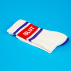 Crew socks, white cotton with blue stripes and red box logo, folded flat on blue surface