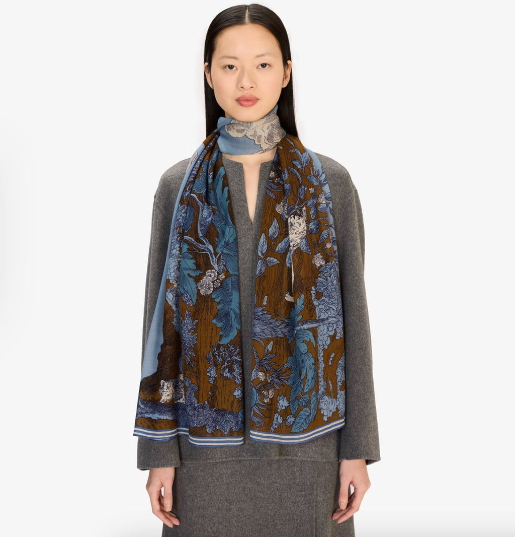 Scarf draped around model's neck, brown and blue floral jungle print with striped border