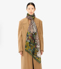 Scarf draped around model's neck, khaki base with leopard and floral jungle print, fringed edges