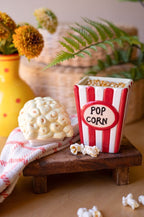 Ceramic popcorn canister red-and-white striped with matching corn kernel lid on rustic wooden riser