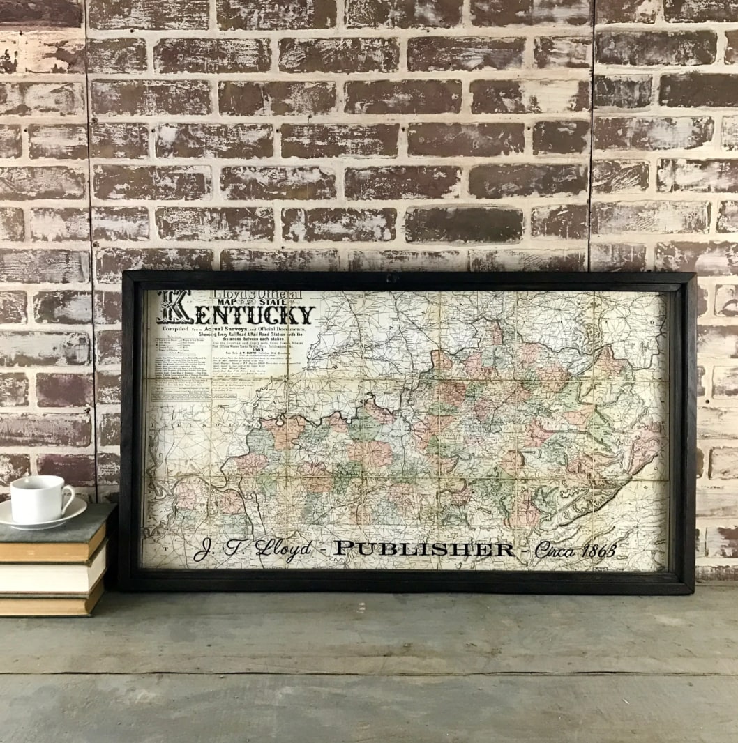Framed vintage Kentucky 1863 map print, black wood frame, horizontal orientation, leaning against brick wall