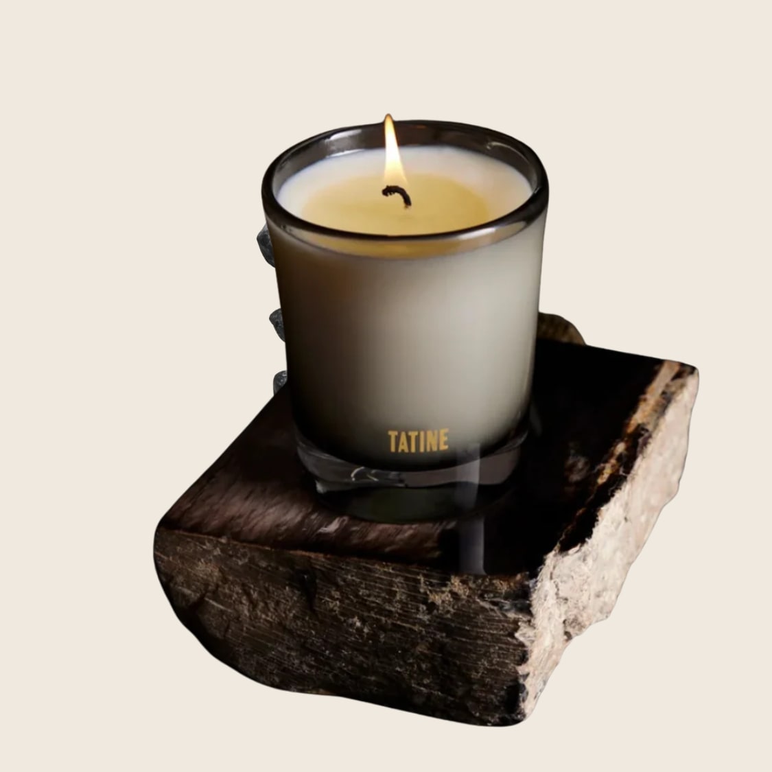 Candle in frosted glass vessel, lit flame, displayed on rustic dark wood slab