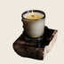 Candle in frosted glass vessel, lit flame, displayed on rustic dark wood slab