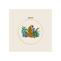 Cross stitch embroidery hoop, completed cheetah amid tropical foliage, natural wood frame, front-facing
