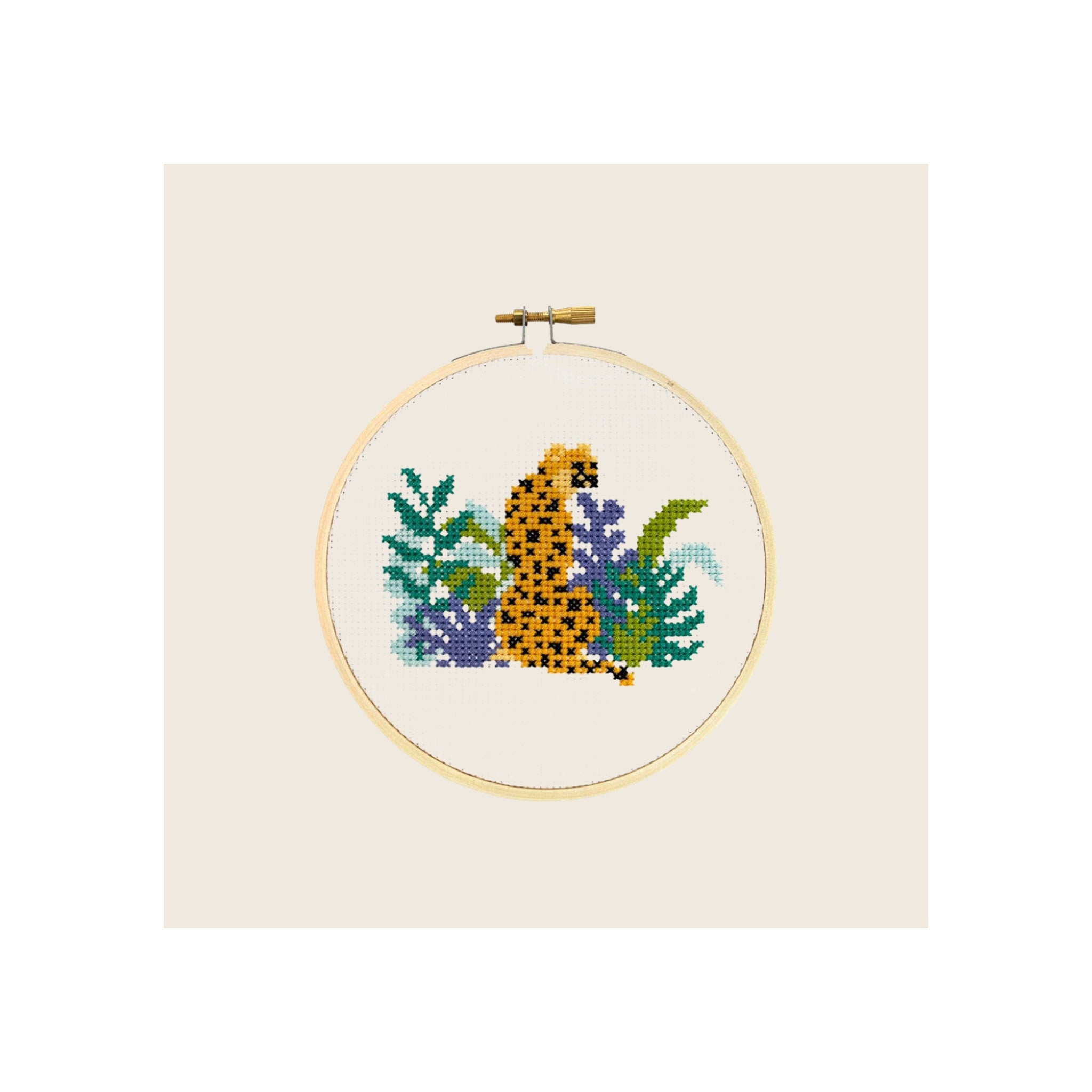 Cross stitch embroidery hoop, completed cheetah amid tropical foliage, natural wood frame, front-facing